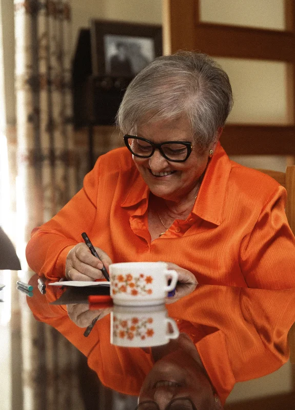 Mi madre, sonriente, escribiendo a mano junto a una taza de café